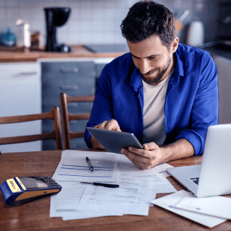Pessoa fazendo contas em mesa com papéis, computador, tablet e máquina SafraPay