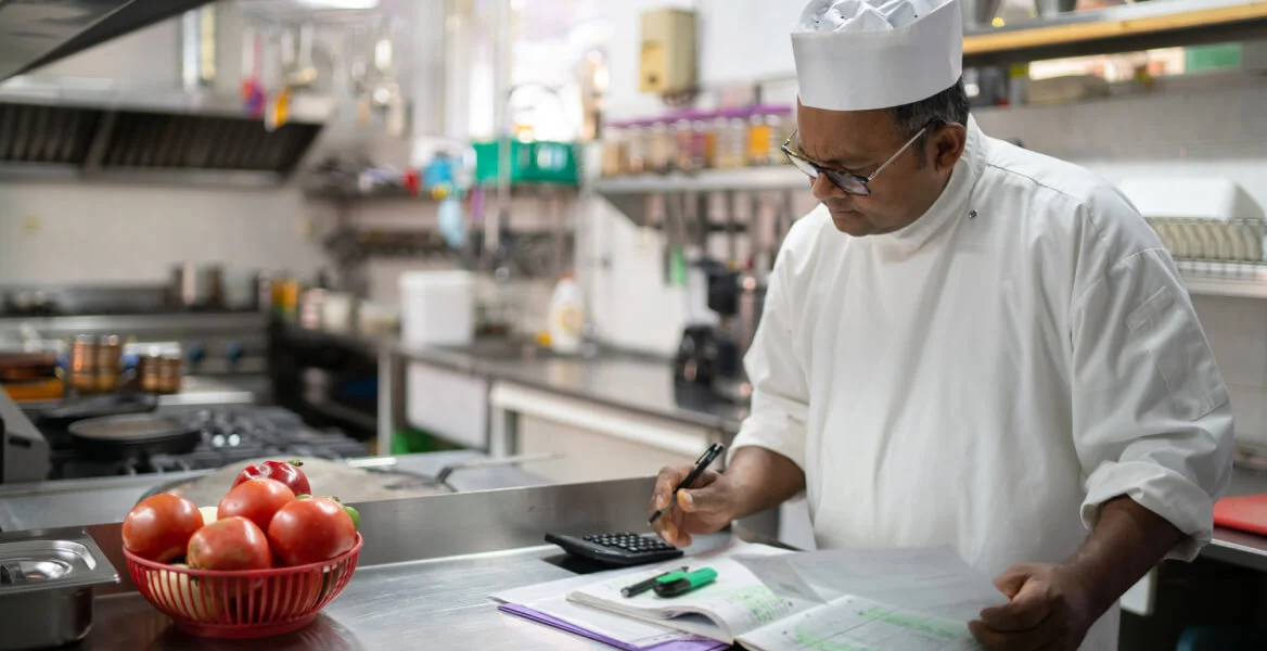 Imagem de um chef de cozinha fazendo contas e anotações.