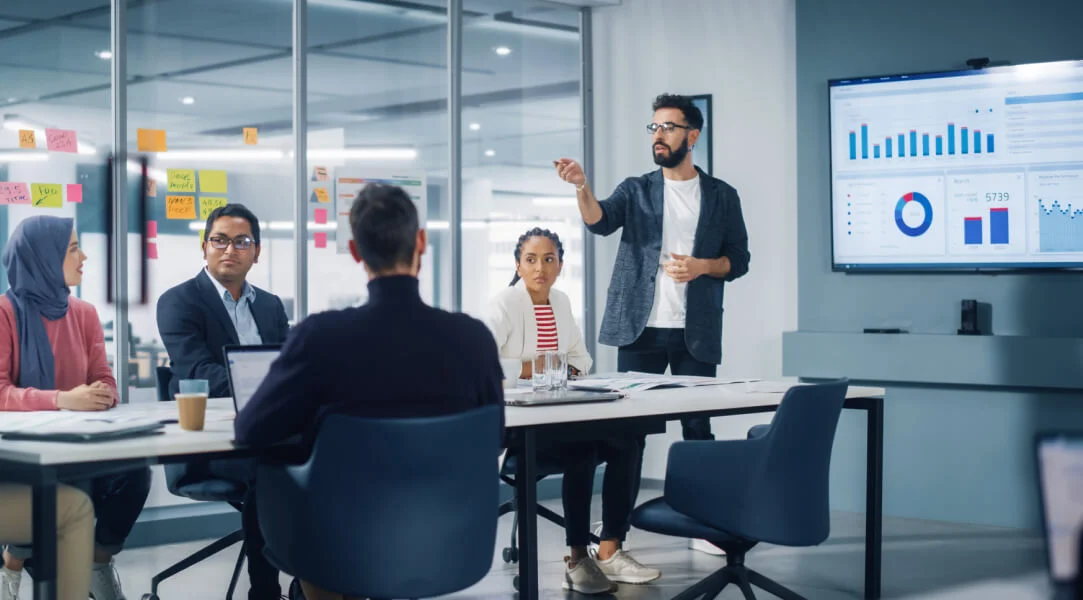 Sala de reunião com um homem apresentando gráficos de resultados.