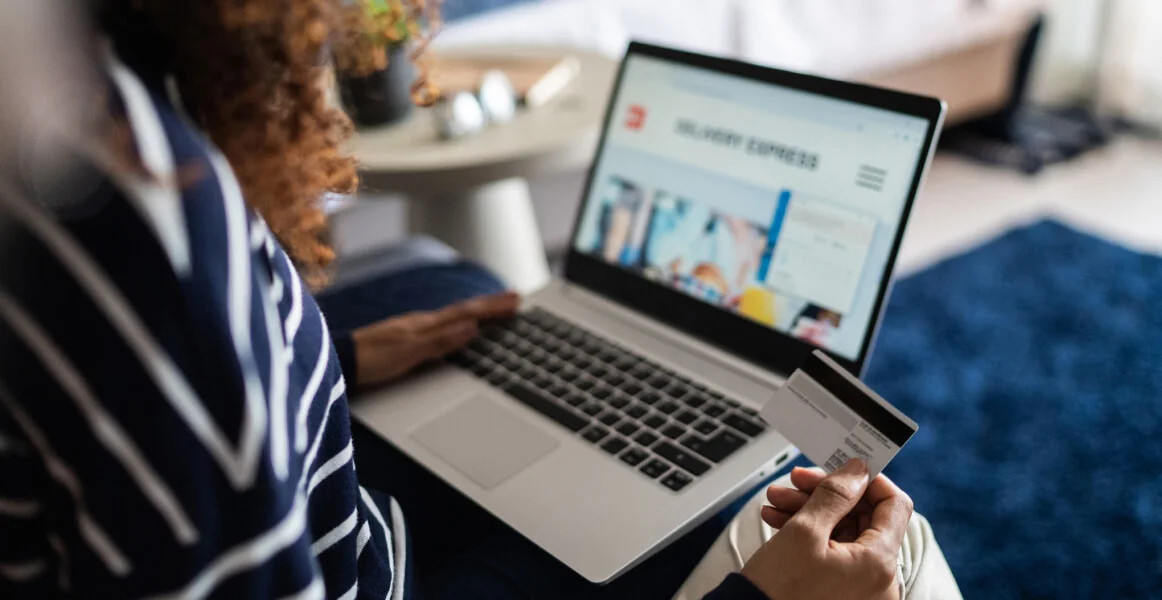 Mulher fazendo uma compra online no computador com o cartão na mão.